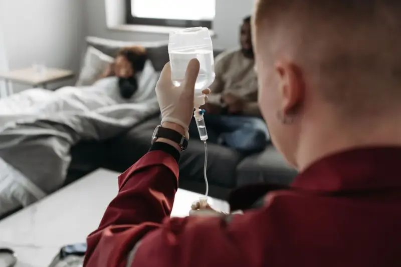 Clinician holding up an IV bag for a patient resting on a sofa at home