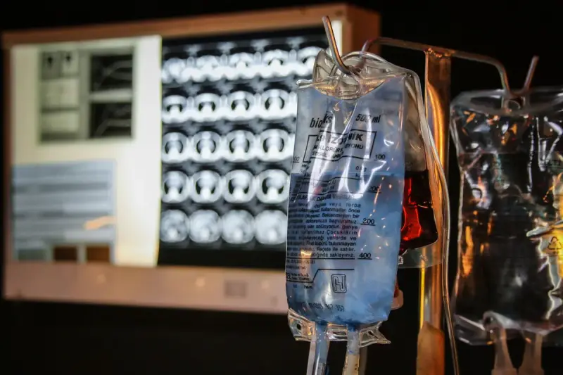 Bags of intravenous fluid hanging from a stand in front of lit imaging screens