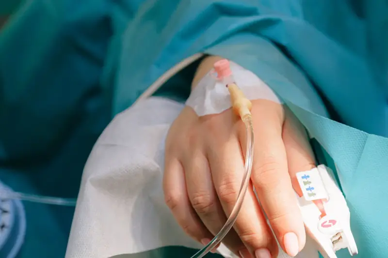 Patient's hand with an IV cannula and a pulse oximeter clip on a blanket