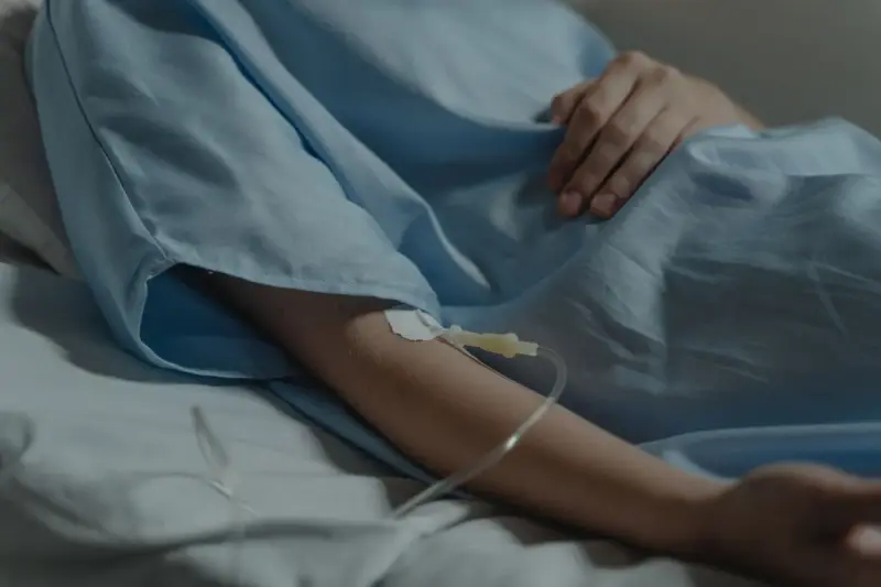 Patient's arm with an IV line resting on a pale blue hospital blanket