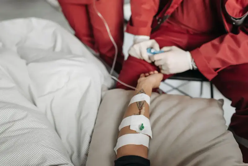 Gloved hands adjusting an IV line and tape on a patient's forearm