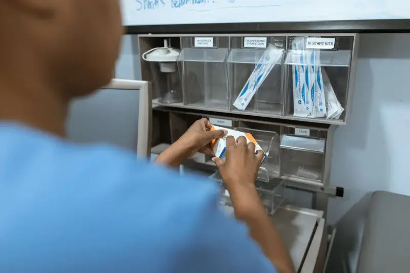 Nurse in blue scrubs taking IV supplies from labeled bins on a supply shelf
