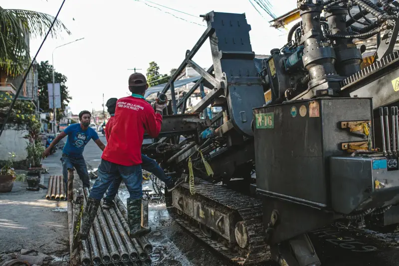 Crew guiding drill rods into a tracked horizontal drilling rig on a city street