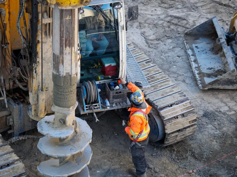 Worker in orange hi-vis beside a tracked drilling rig with an auger