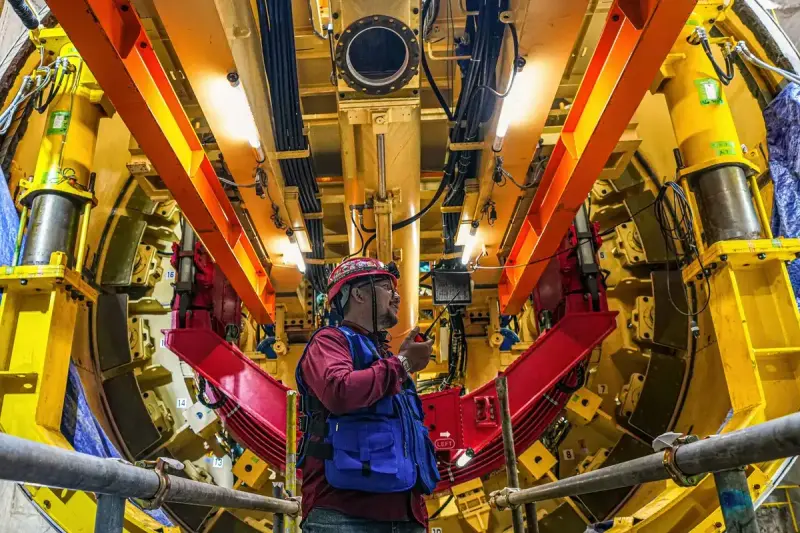 Engineer with a radio standing inside the yellow and red frame of a tunnel boring machine