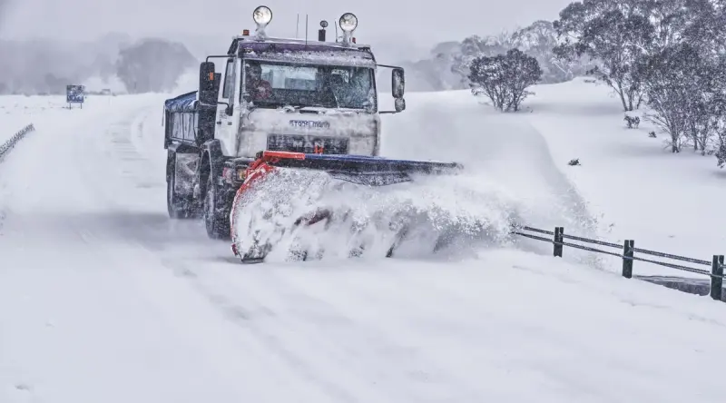 Heavy snow plow truck pushing a wave of snow along a rural road