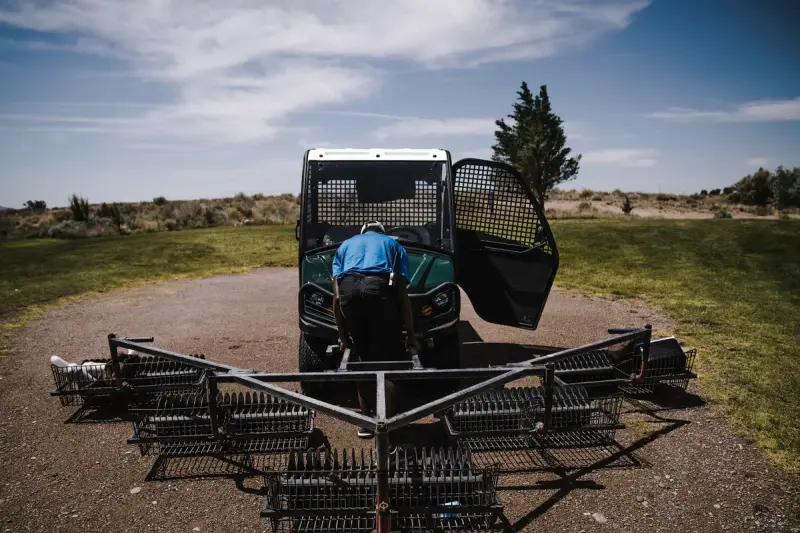 Grounds worker servicing a utility vehicle and drag mat on a golf course