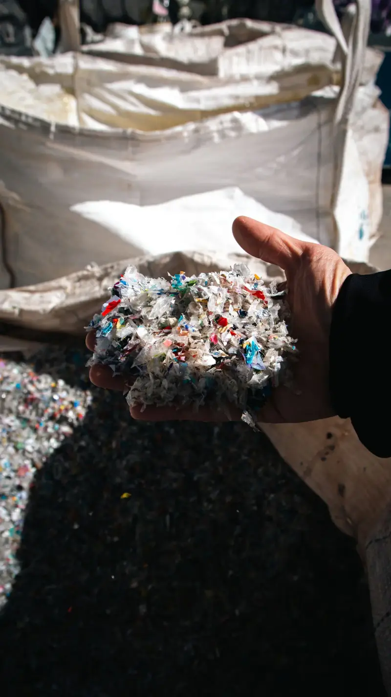 Hand holding recycled plastic granules in sunlight at a recycling facility