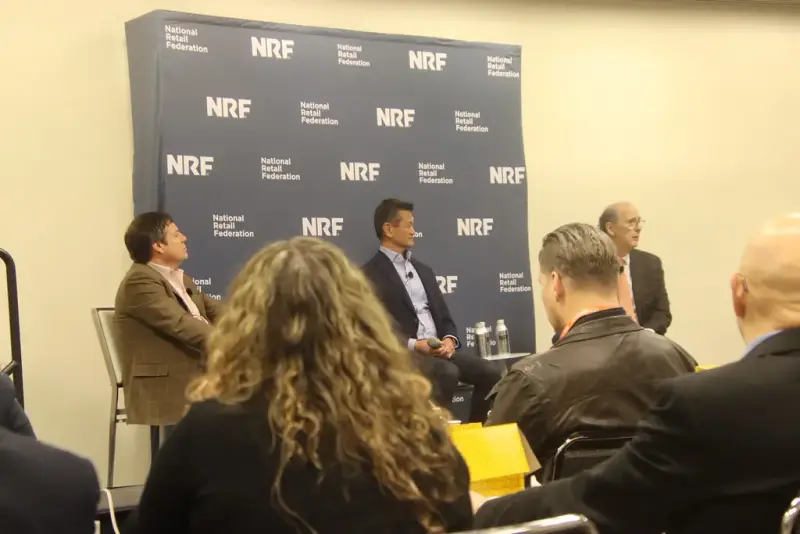 Panel discussion in front of an NRF backdrop with an audience listening