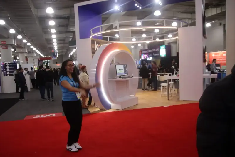 Expo hall aisle with red carpet and a glowing ring-shaped stand at the Javits Center