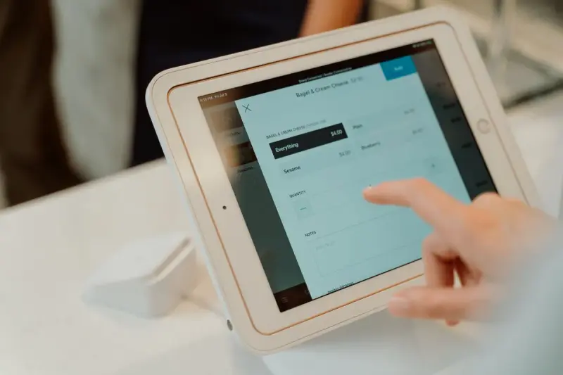 Finger tapping an order on a tablet point of sale screen on its stand