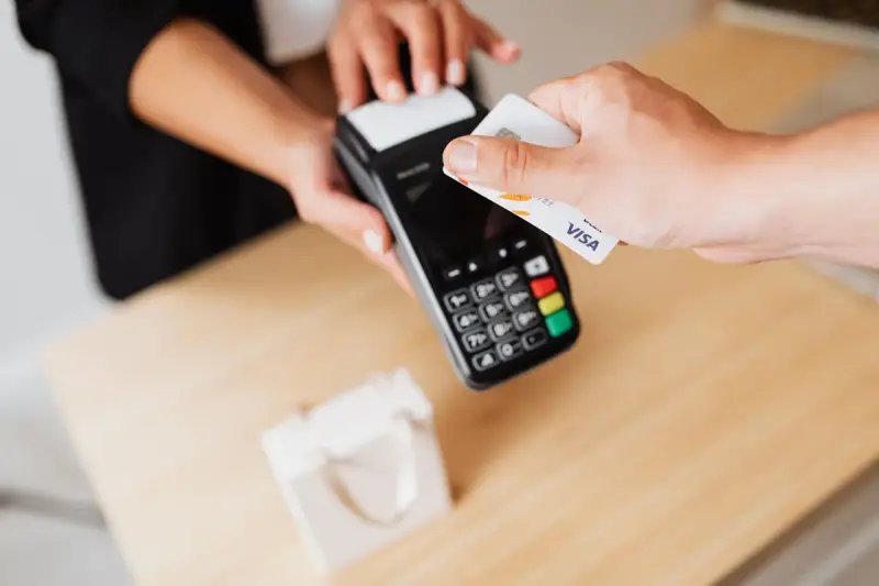 Customer tapping a card on a handheld payment terminal held over a wooden counter