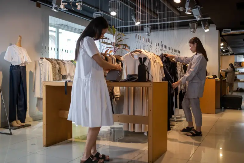Two women browsing clothing on rails and tables in a bright modern fashion store