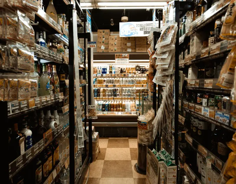 Narrow convenience store aisle packed with bottles, snacks and a lit drinks cooler