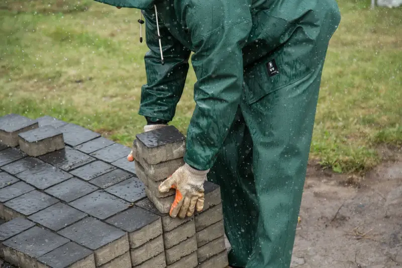 Worker in rain gear setting paving stones on an outdoor job site