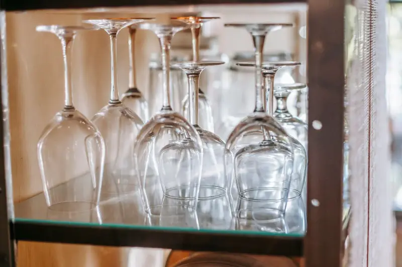 Upside-down wine glasses lined up on a glass shelf in a cabinet