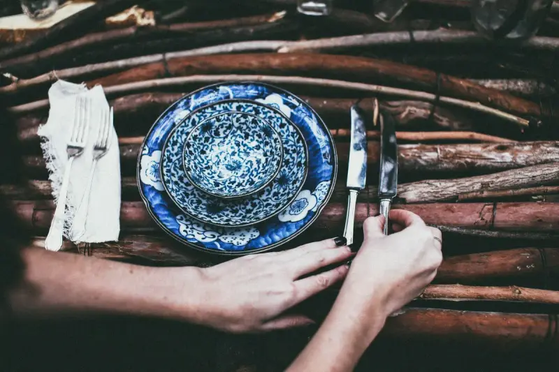 Person placing cutlery beside blue ceramic plates on a rustic wooden table