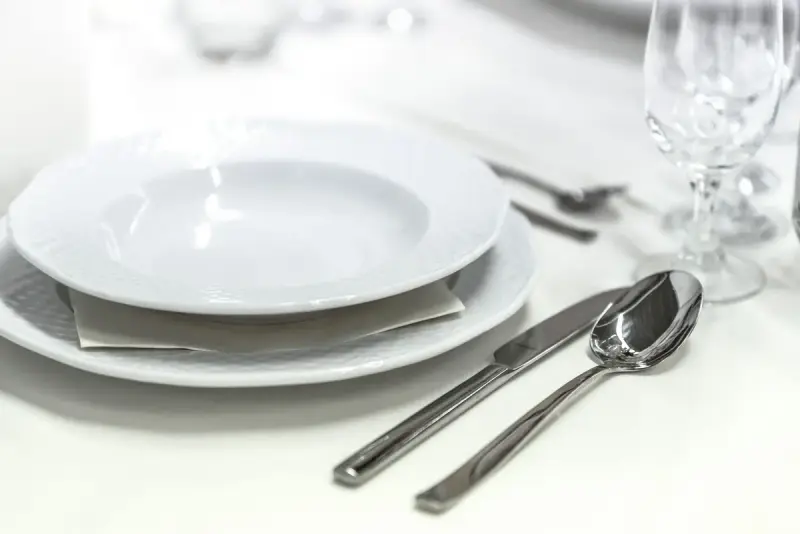 Dining table with white porcelain plates, silver cutlery and wine glasses