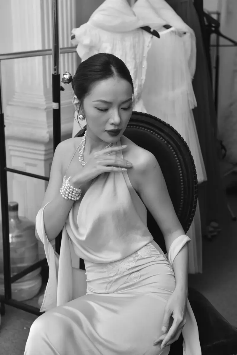 Black and white portrait of a woman in a satin gown with pearl bracelets in an atelier