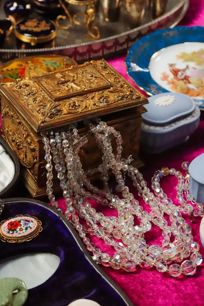 Antique jewelry box spilling crystal beads beside painted porcelain plates on velvet