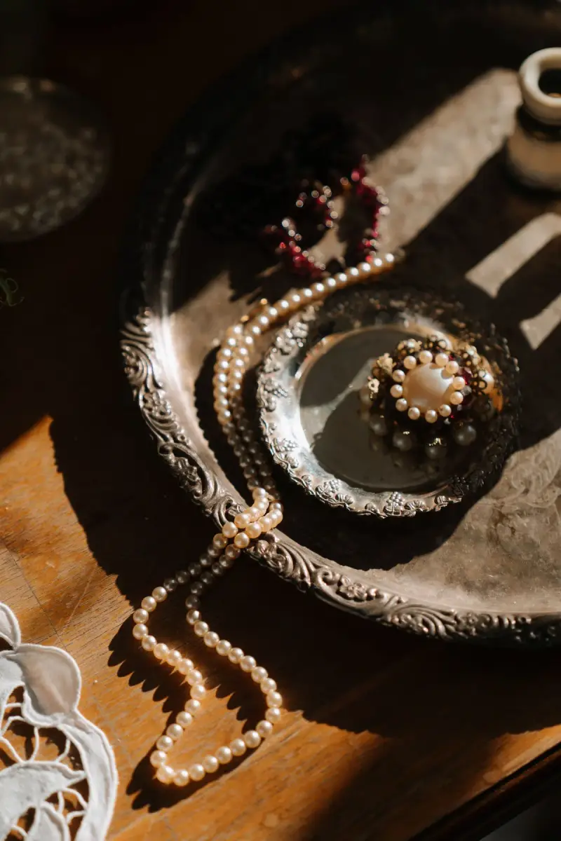 Flat lay of a vintage silver tray with a pearl brooch, pearl strands and garnet beads