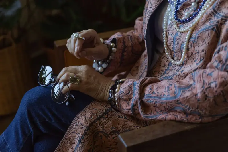 Elderly woman wearing layered jewelry and holding eyeglasses