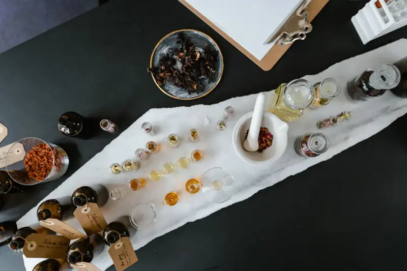 Overhead view of glass bottles of yellow and orange oils with botanicals on a work table