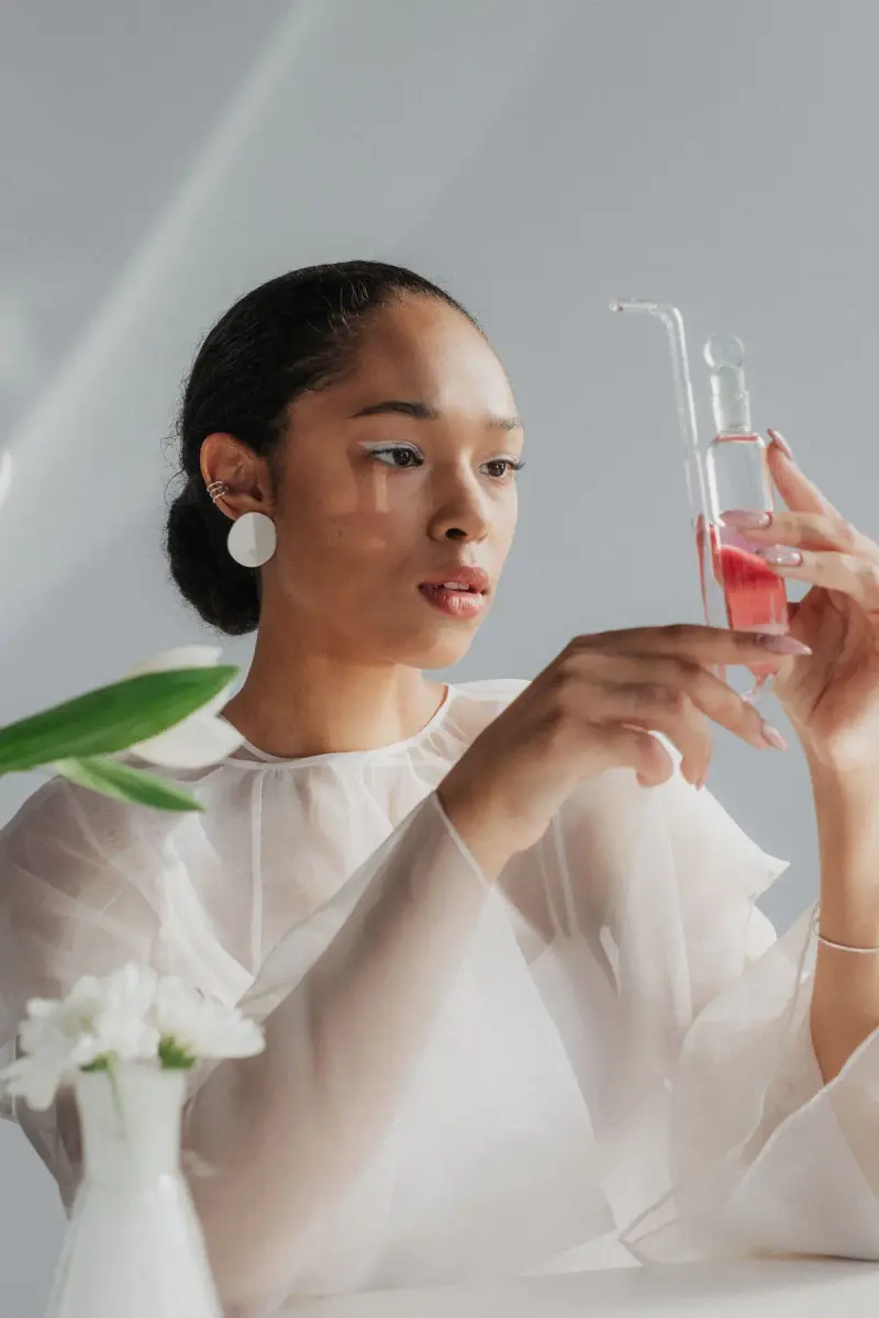 Woman in a sheer white blouse studying a glass tube of pink liquid