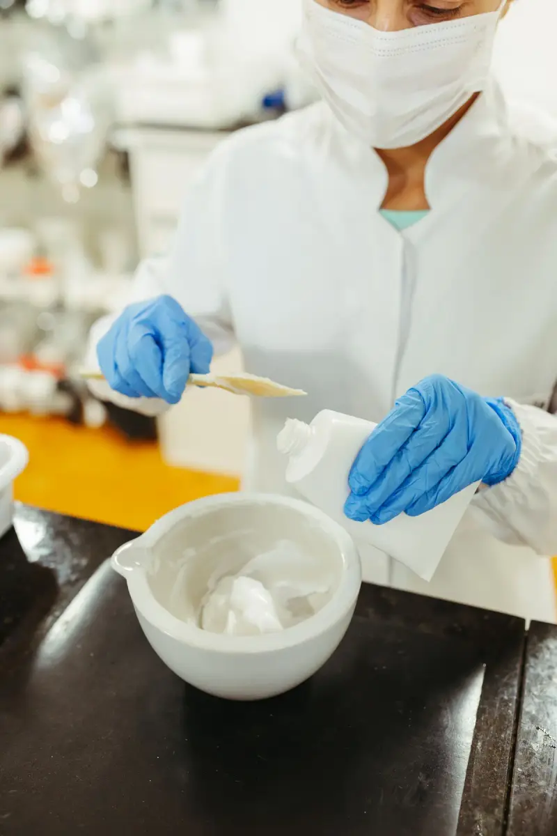 Lab technician in gloves mixing white cream in a ceramic bowl