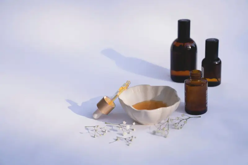 Amber glass bottles, a ceramic bowl of oil and a dropper on a pale lavender surface