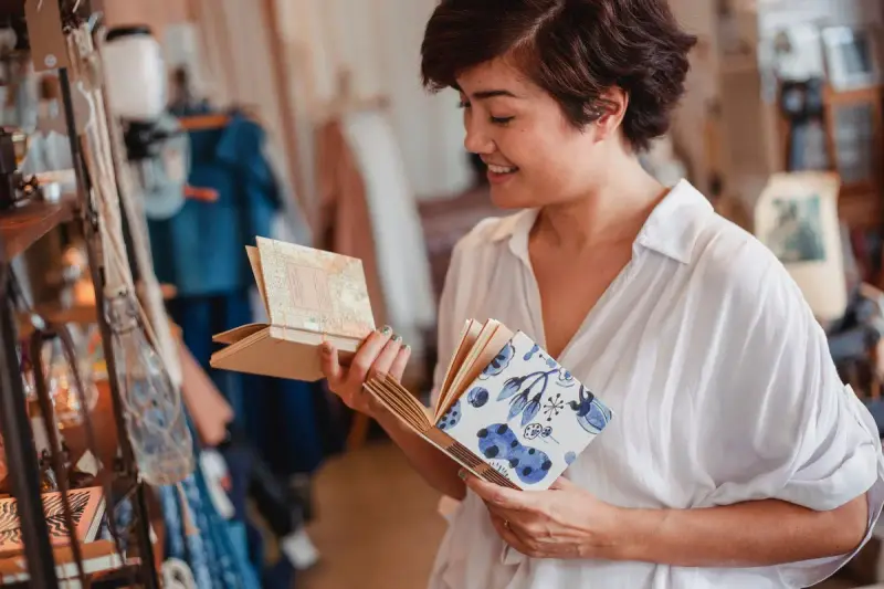 Smiling woman comparing patterned notebooks in a gift and souvenir store