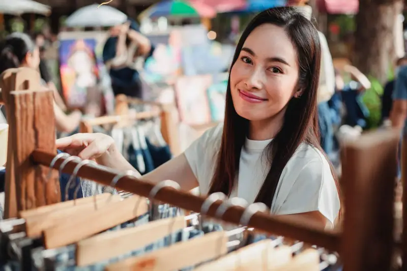 Smiling woman shopping a rack of clothing on wooden hangers at an outdoor market