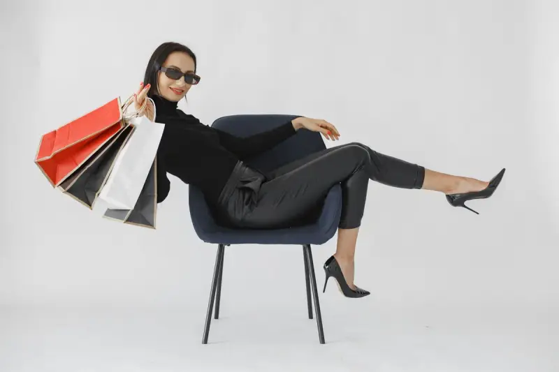 Woman in black with sunglasses lounging in a chair holding colorful shopping bags