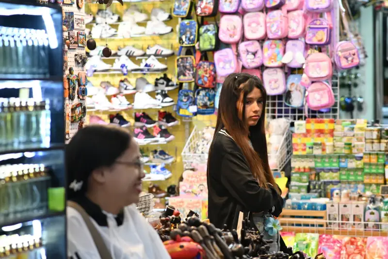 A young woman browsing a market stall full of colorful backpacks