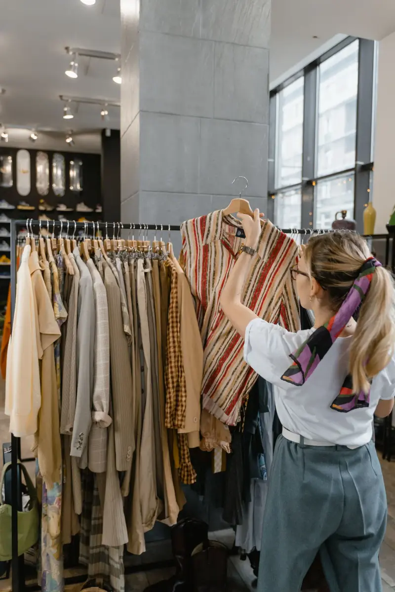 Woman with a silk hair scarf pulling a striped shirt from a full rack of neutral clothing