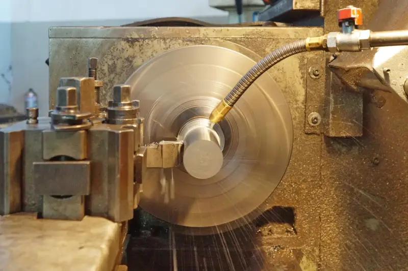 Lathe turning a shiny steel part at speed while a coolant nozzle sprays the cut