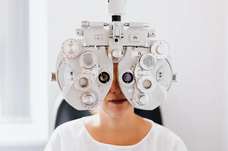 Patient in a white shirt looking through a phoropter during a refraction exam