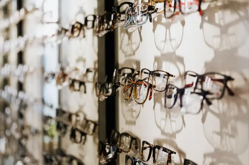 Rows of eyeglass frames mounted on a white display wall in an optical store