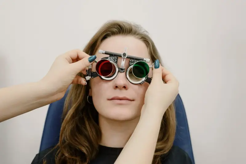 Eye care professional fitting a trial frame with red and green lenses on a young woman