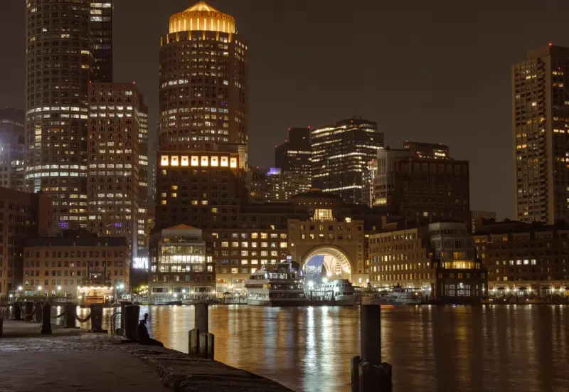 Boston waterfront towers and harbor lit at night, seen from Fan Pier Park