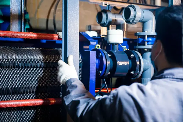 Worker in blue sleeves inspecting pipework in an industrial plant