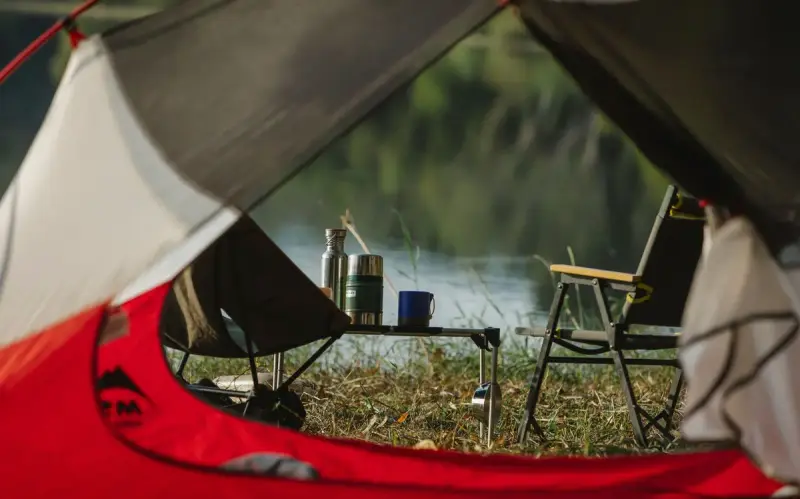 View from an open tent of folding camp chairs and a table beside a lake