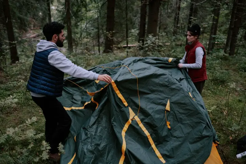 A man and a woman assembling a green tent in a forest