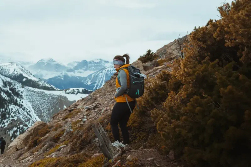 Woman in sportswear with a backpack trekking below snow-capped mountain peaks