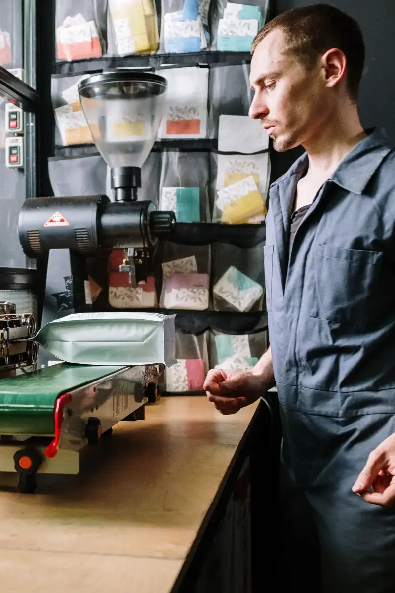 Worker in coveralls operating a bag sealing machine at a coffee roasting plant