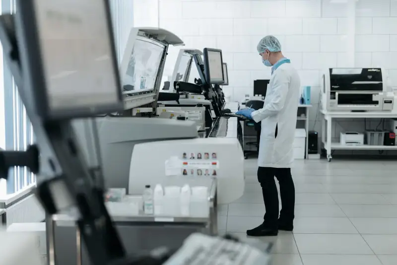 Technician in a hairnet and lab coat running an automated analyzer in a modern laboratory