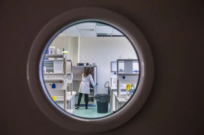 Scientist in a lab coat seen through a round porthole window into a clean laboratory