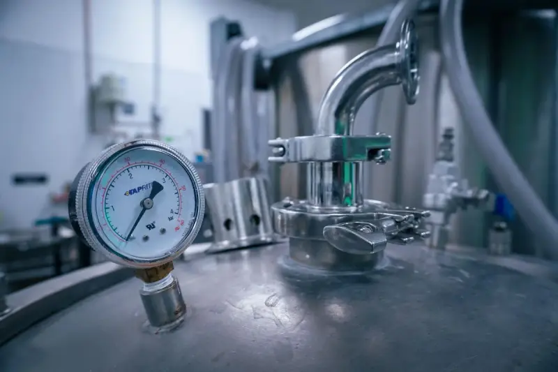 Pressure gauge and sanitary clamp fittings on top of a stainless steel process tank