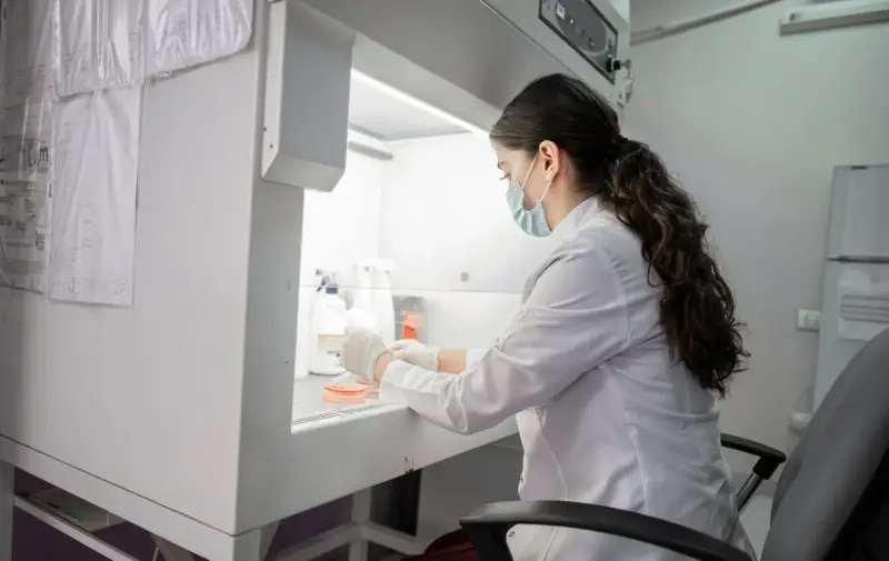 Scientist in a lab coat and mask working inside a biosafety cabinet
