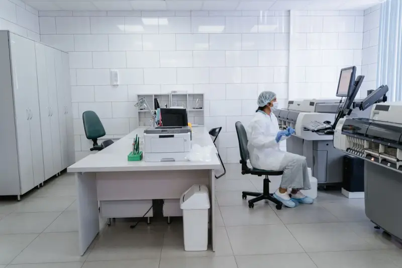 Gowned lab technician working at an instrument workstation in a bright white laboratory